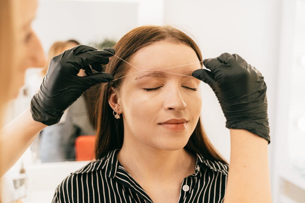 A woman receives precise eyebrow threading in a modern salon setting.