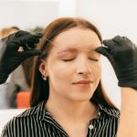 A woman receives precise eyebrow threading in a modern salon setting.